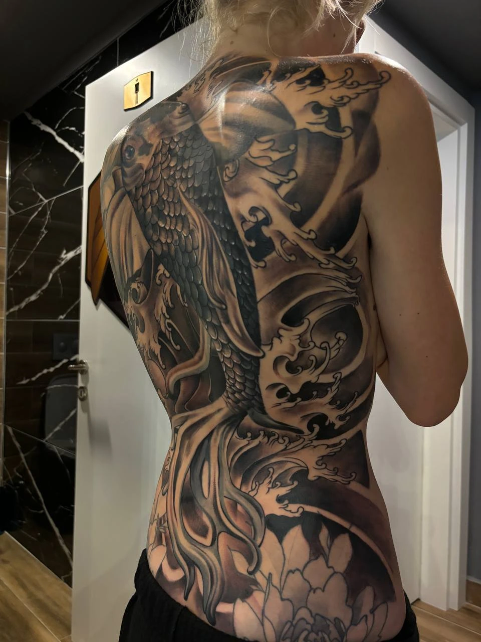 Black-and-grey koi swimming through Japanese waves with peony, full back piece