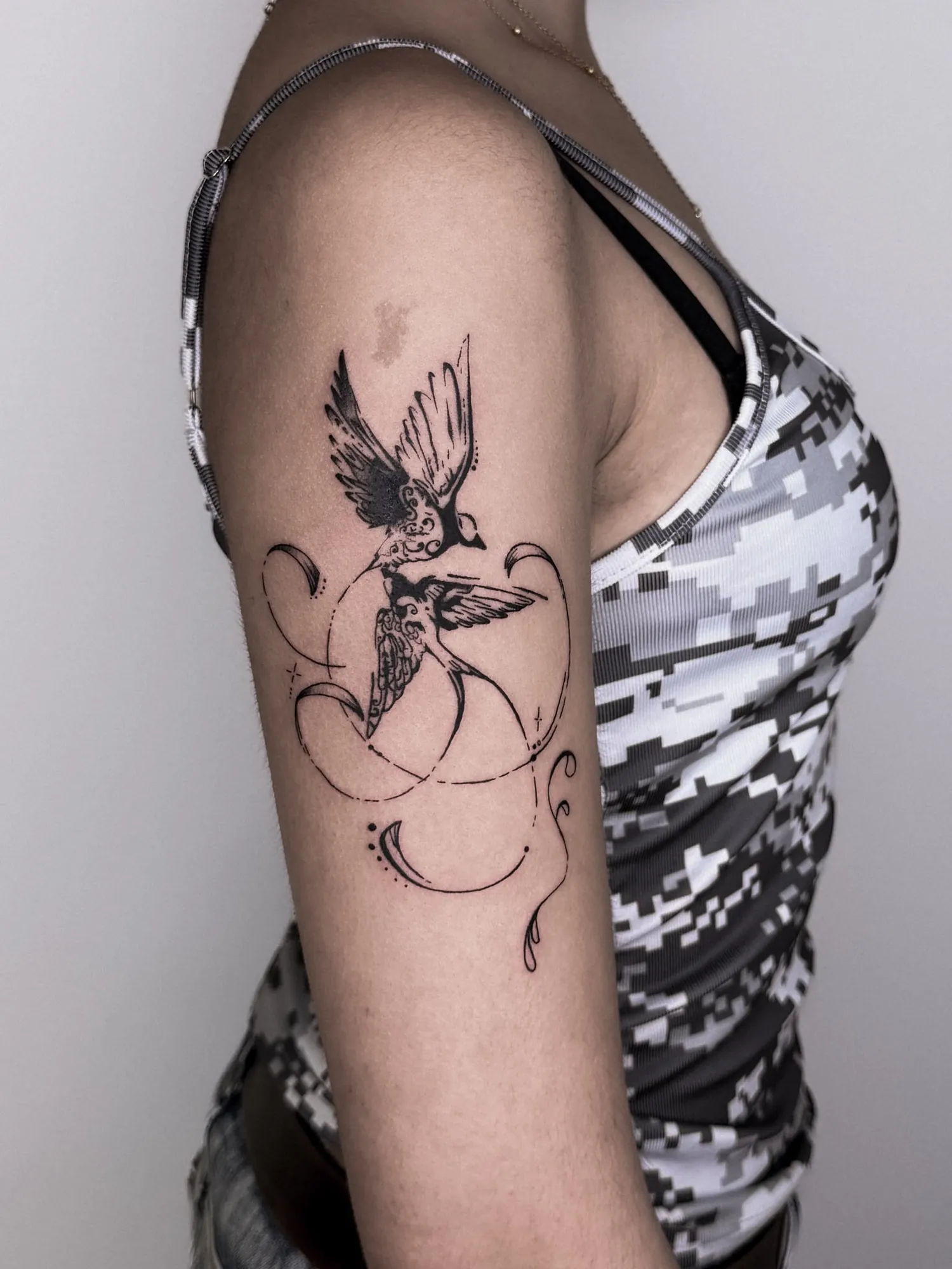 black & grey two swallows in flight with ornamental swirls, crescents and dots on outer upper arm