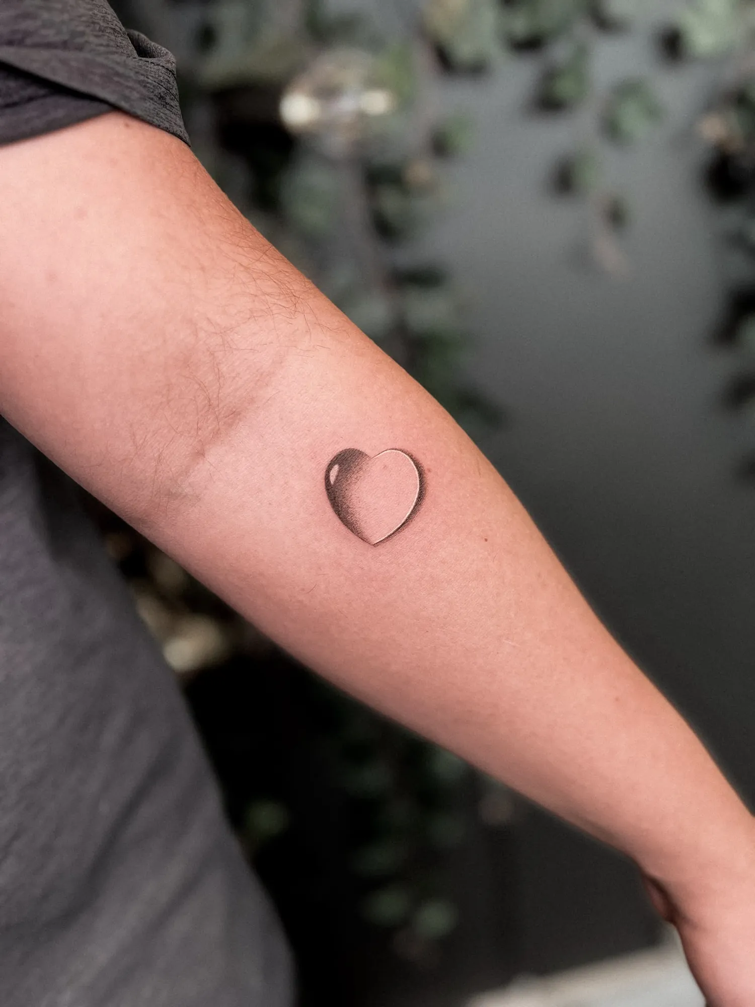 small black & grey realistic glass-like heart with highlight and shadow on inner forearm