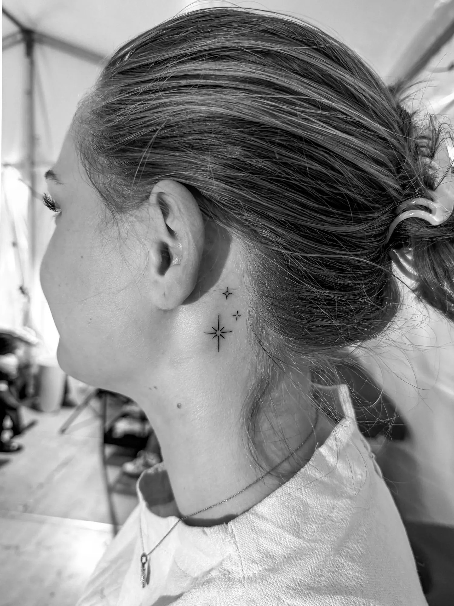 three small fineline sparkle stars of different sizes behind the ear, black and white photo