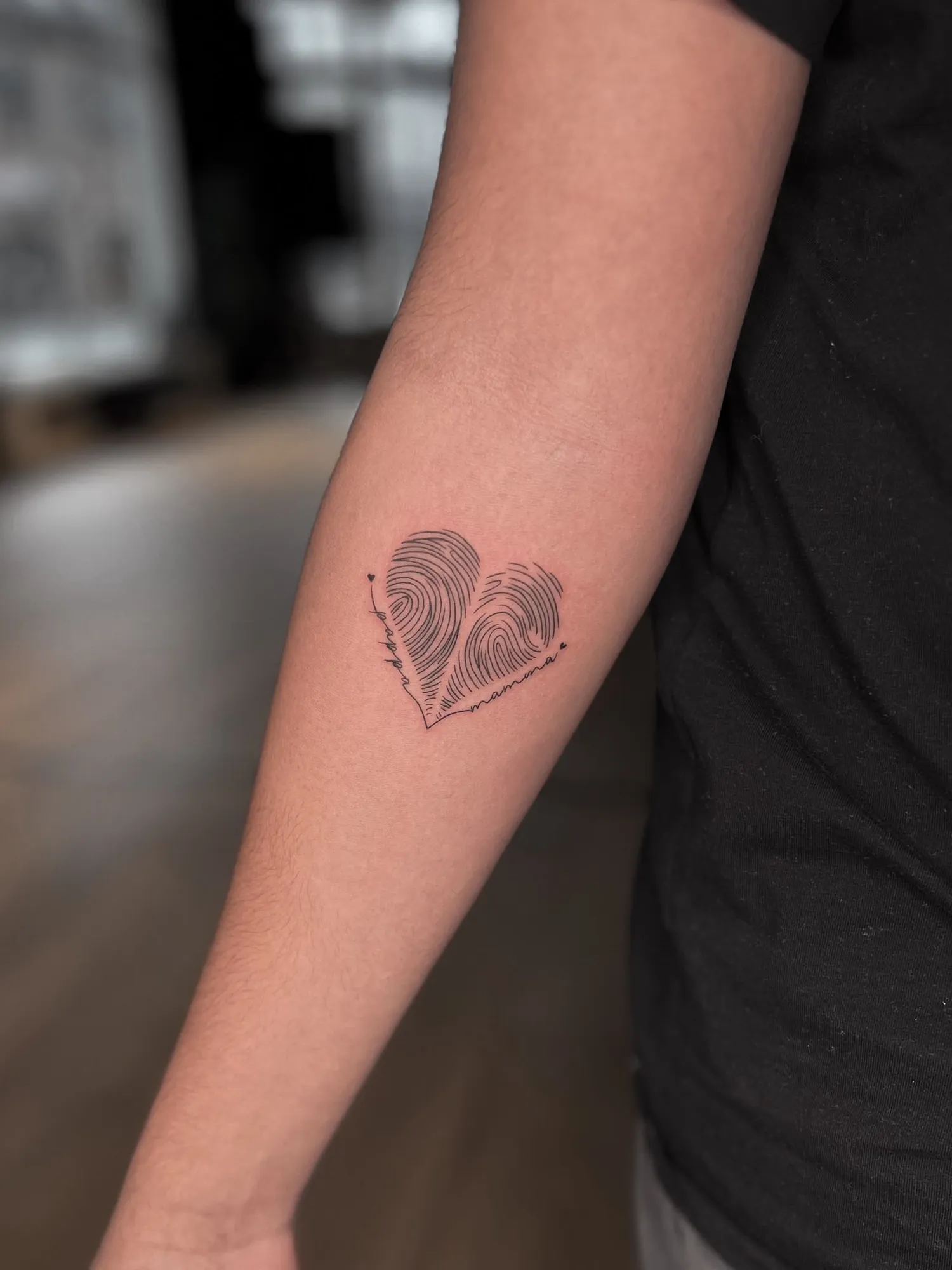 fineline heart made of two fingerprints with tiny script 'pappa' along the left edge and 'mamma' along the right edge, on the inner forearm