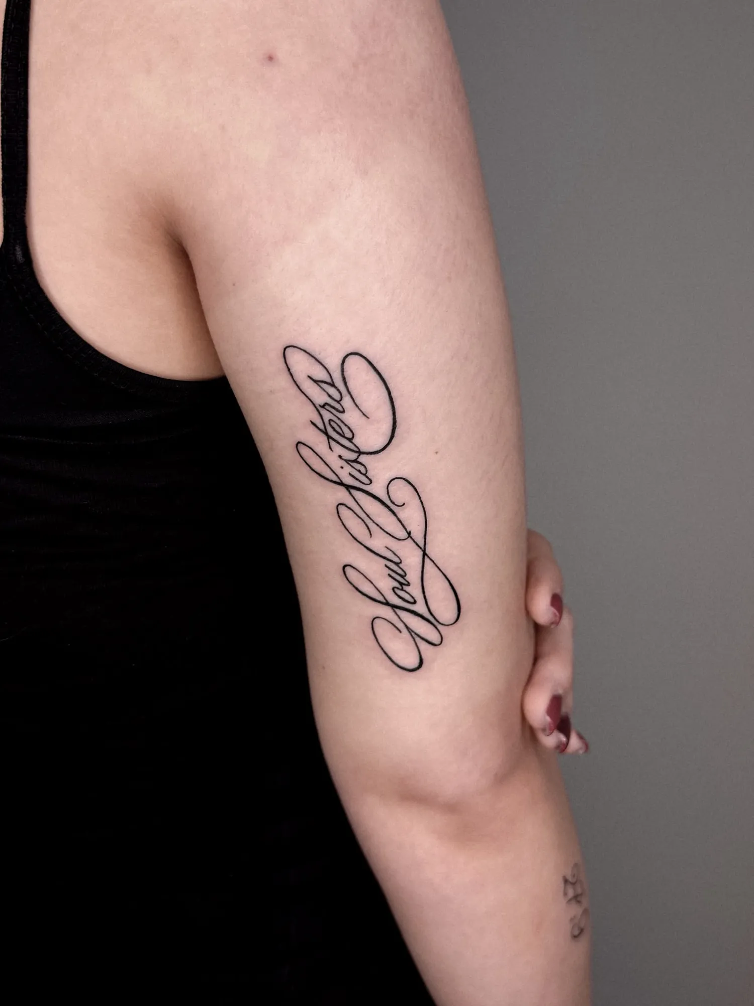 ornate calligraphic script 'Soul Sisters' with flourishes on back of upper arm, grey studio backdrop