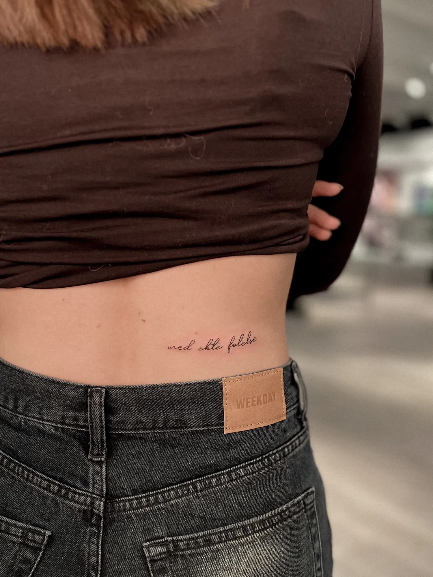 thin cursive script 'med ekte følelse' across lower back above waistband