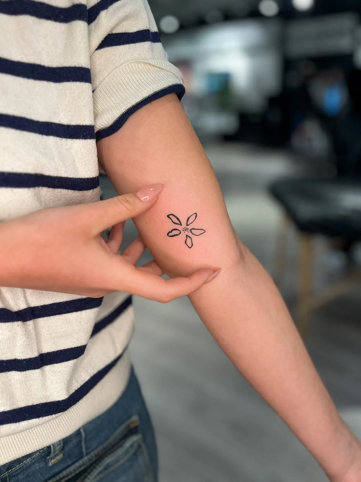 small bold-outline five-petal flower with dotted centre on inner arm just above elbow crease