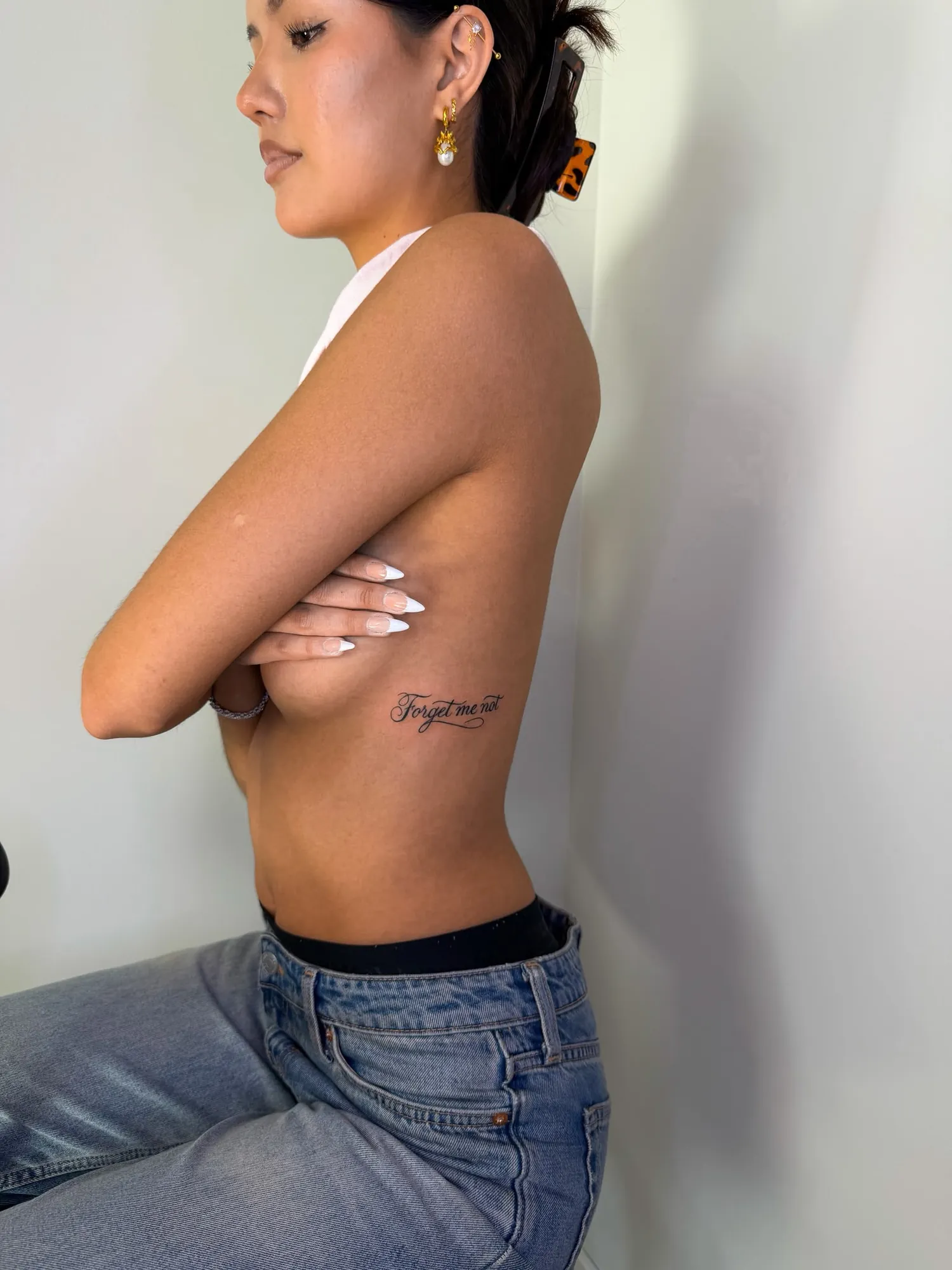 flourished script 'Forget me not' on side of ribcage, person in profile with arms crossed