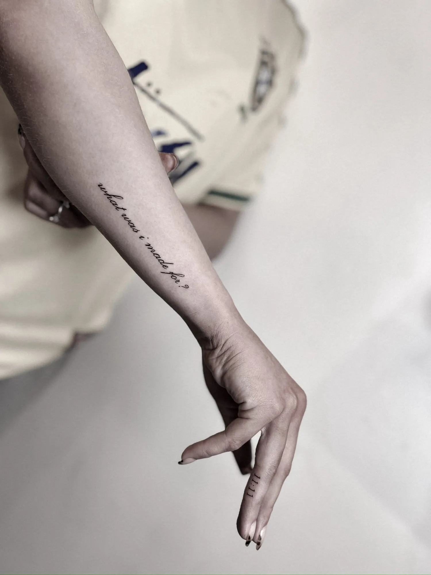 fine cursive script 'what was i made for?' along inner forearm, plus small '11:11' on side of index finger