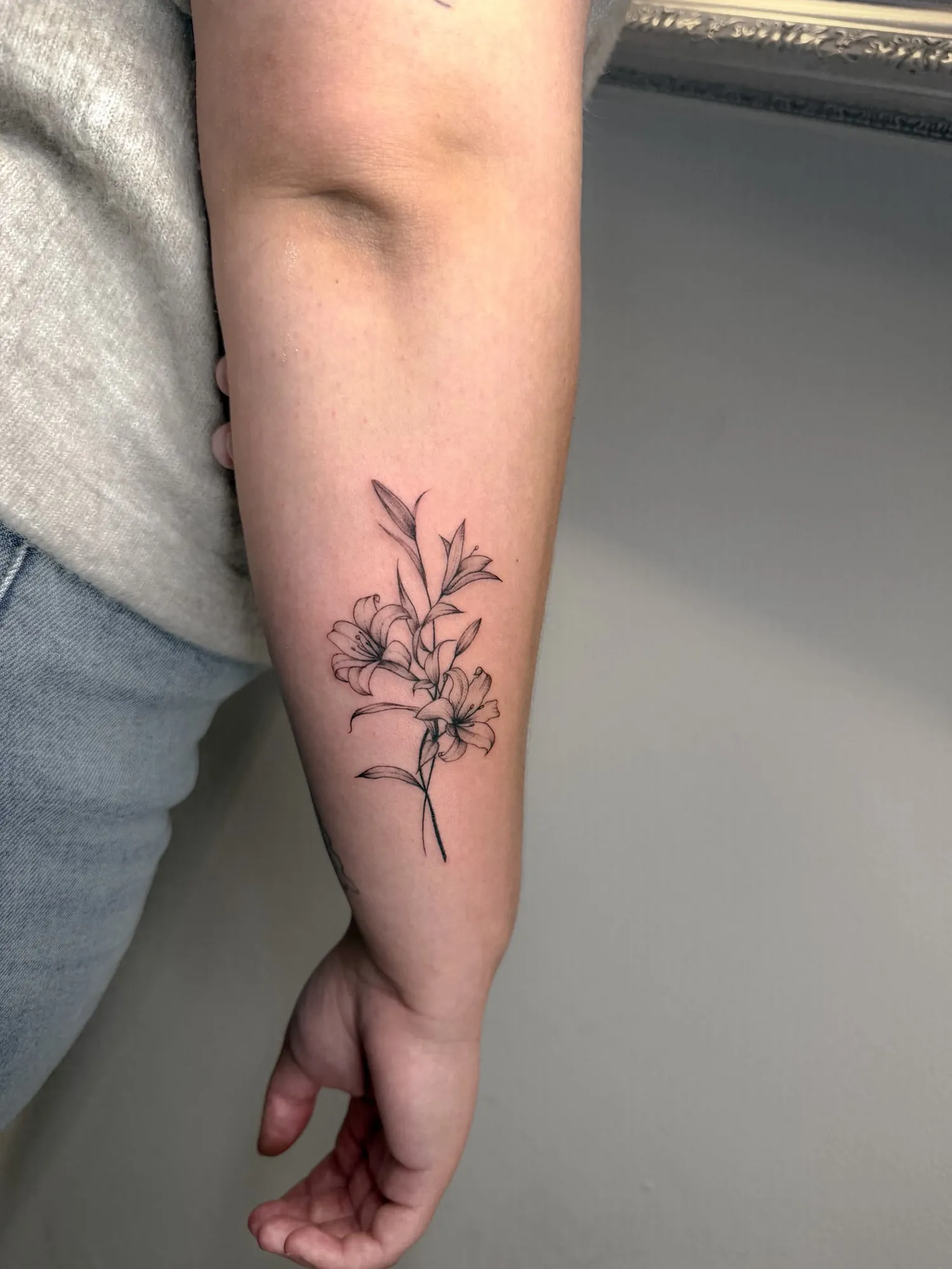 black & grey fineline lily sprig with three blooms and leaves on inner forearm