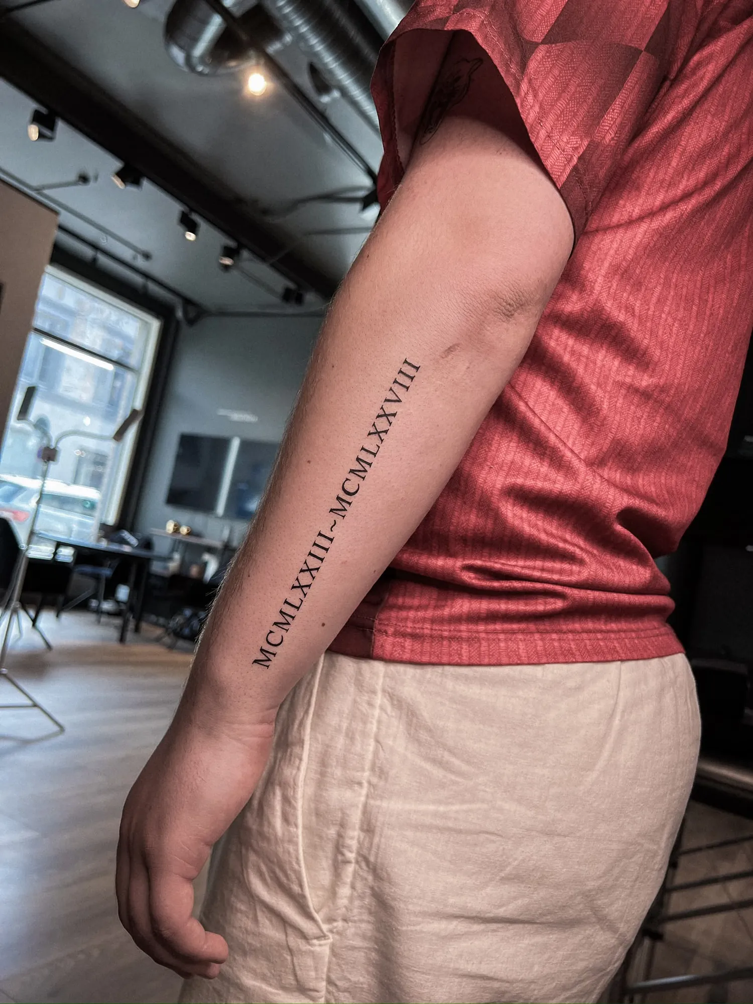 serif Roman numerals 'MCMLXXIII~MCMLXXVIII' in one line along outer forearm