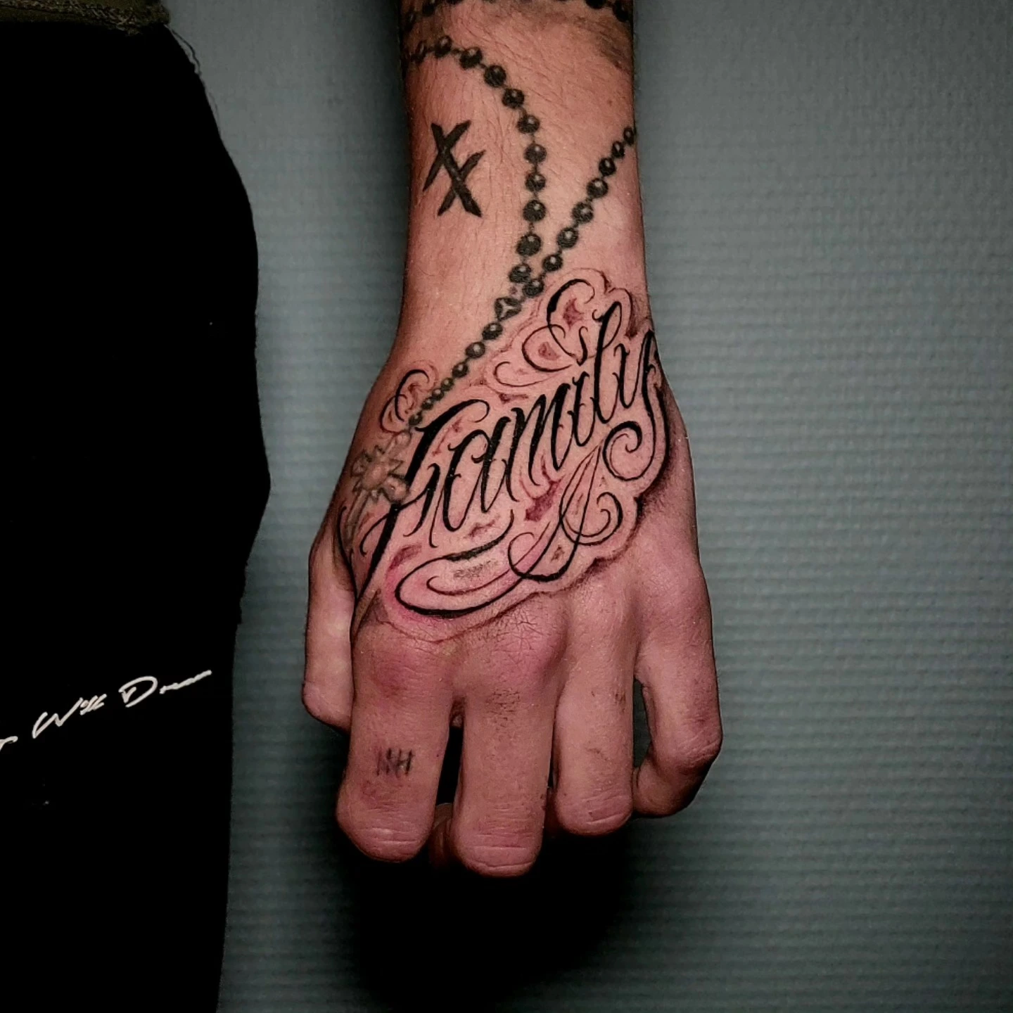 'Family' chicano filigree on hand below rosary chain