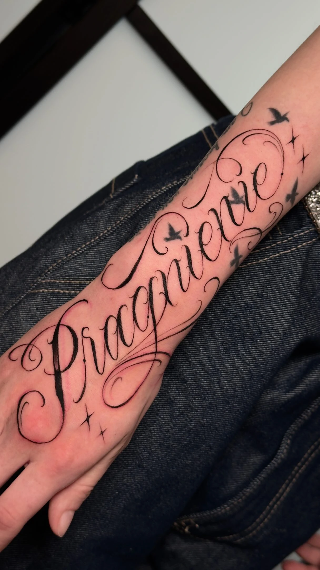 'Praguenenne' (or similar) cursive script with birds/stars on hand-forearm
